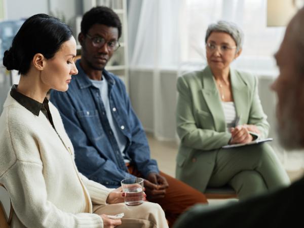 A therapist and group therapy participants wait for a woman in the group to compose herself and speak