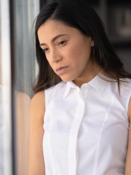 A depressed woman leaning her shoulder against a window and looking outside