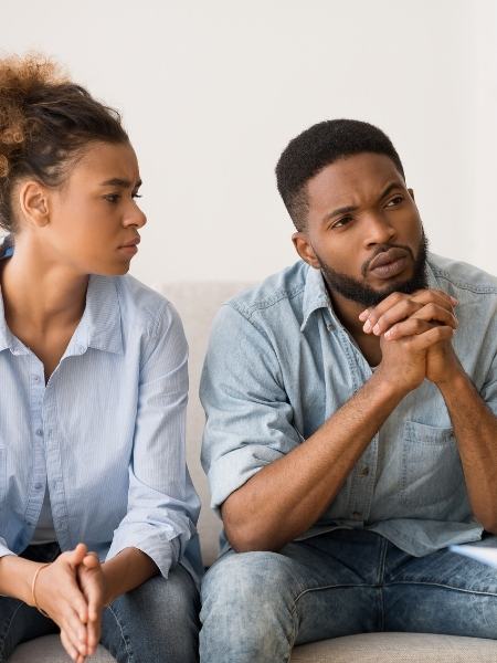 A man with folded hands listens to a therapist as his partner looks at him