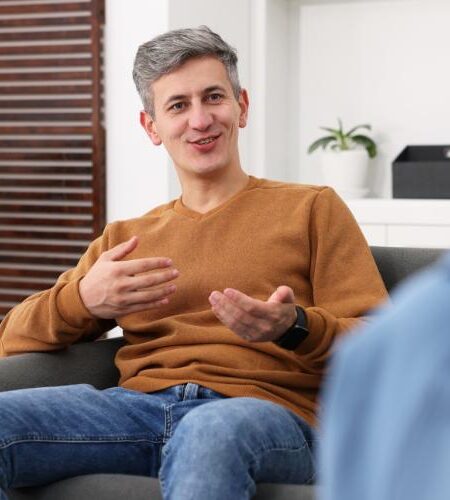 A man sitting on a couch, smiling, and talking during mental health therapy