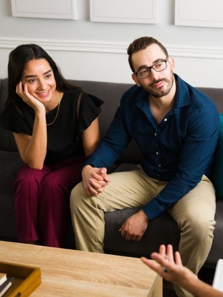 A couple sitting, holding hands, and smiling while listening to a mental health therapist